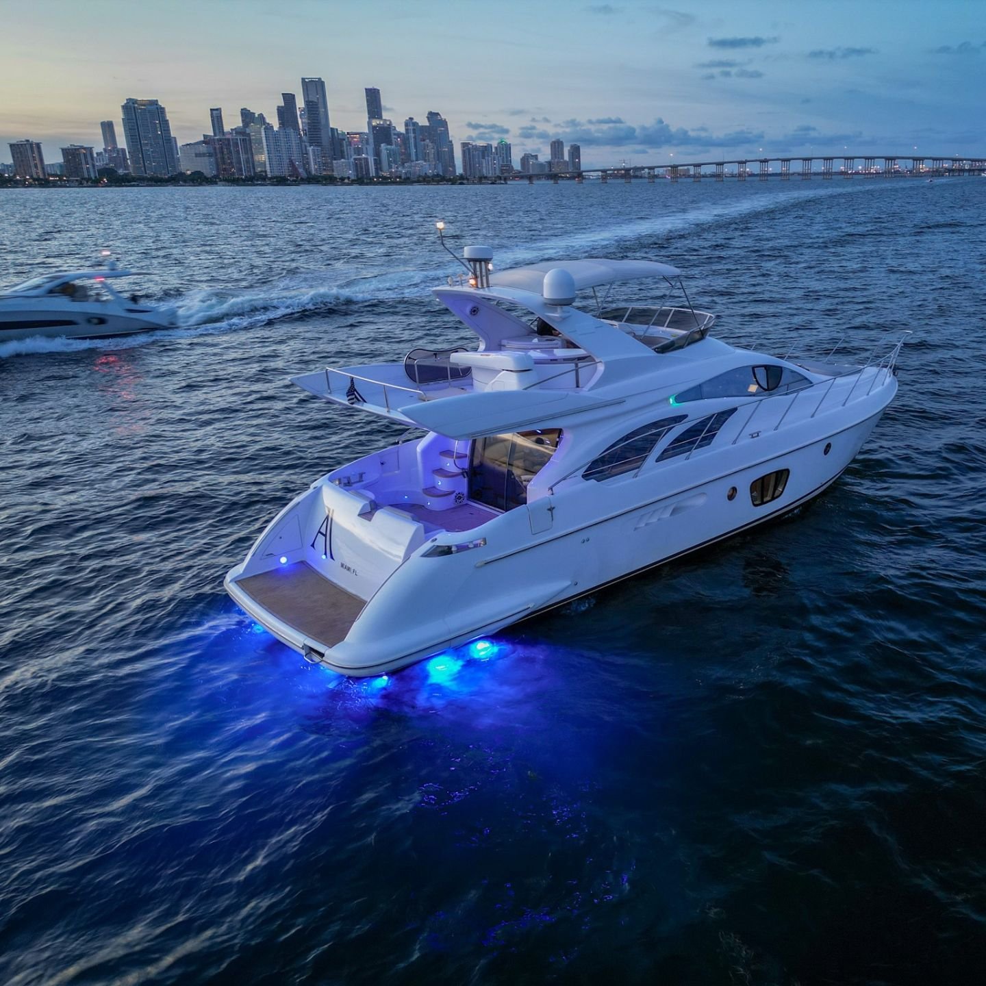 Flybridge yacht with underwater lights cruising Biscayne Bay at dusk