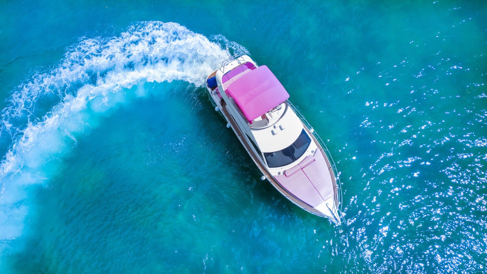 Aerial view of a yacht with a pink bimini cruising turquoise water